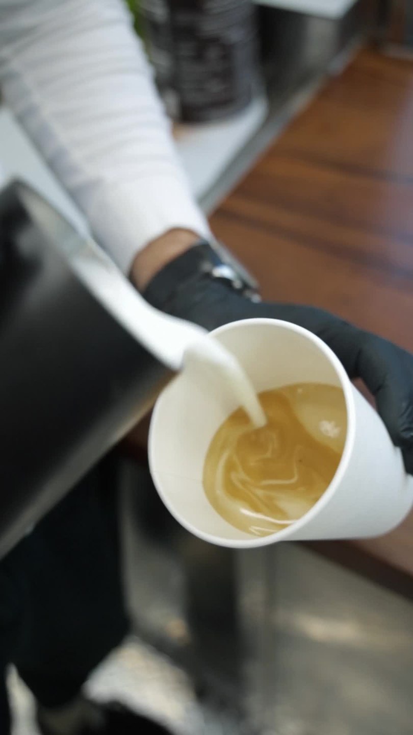 Gloved hands pouring milk into a cup of coffee